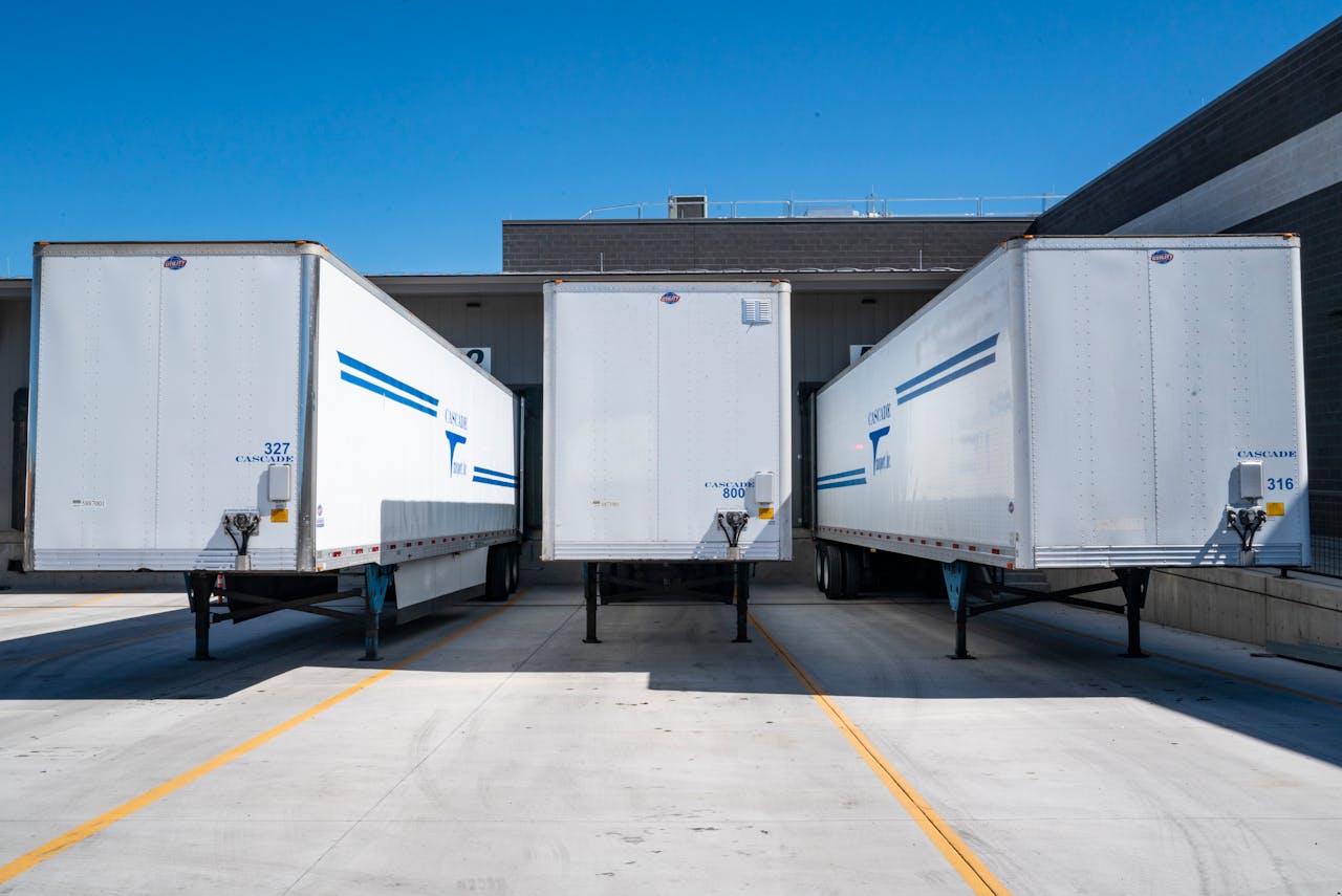 creative-02 Three white cargo trailers parked at an industrial shipping dock under clear blue skies.