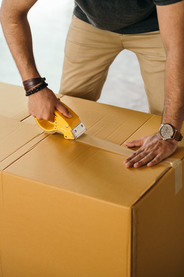 creative Unrecognizable man sealing box with duck tape while preparing for moving out